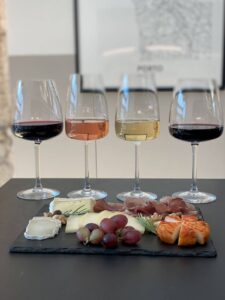 Four wine glasses, two red, one rosé, one white, with a slate platter of cheeses, grapes, walnuts, and cured meats. Perfect f