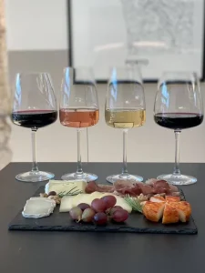 Four wine glasses, two red, one rosé, one white, with a slate board of cheeses, prosciutto, grapes, and walnuts. Perfect for