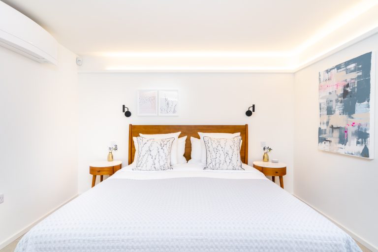 Modern bedroom with a wooden headboard, white bedding, patterned pillows, two round bedside tables, and abstract art.
