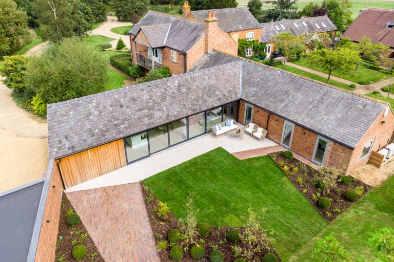 Aerial view of The Barn at 14 Acres, showing the modern extension, patio with outdoor furniture, and lush green lawn.