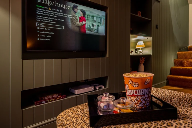 A large TV screen showing "The Lake House" movie on Netflix, with popcorn and sweets on a leopard print ottoman in a luxury l