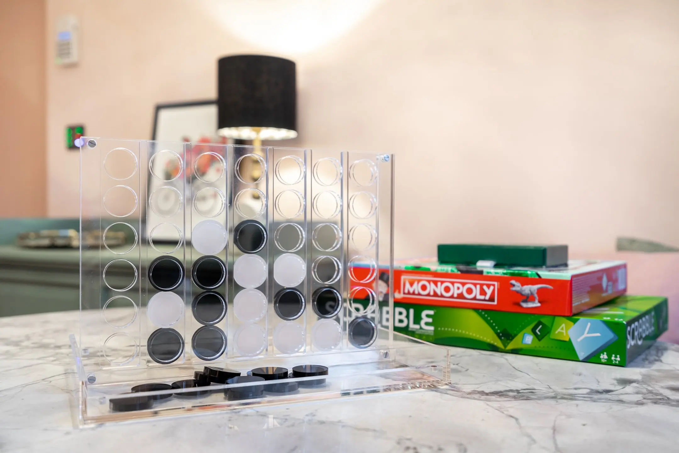 Connect Four game with black and white discs on a marble table, with Monopoly and Scrabble boxes in the background at 14 Acre