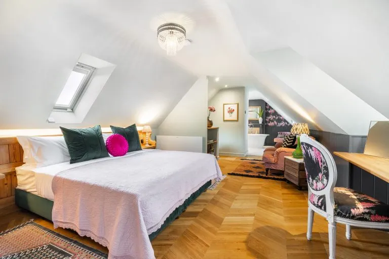 Luxury bedroom at The Loft, 14 Acres, with king-size bed, green and pink cushions, herringbone floor, and roll-top bath.