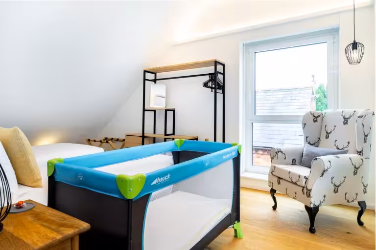 Hauck travel cot in a bright, modern bedroom with a stag-patterned armchair and wooden floor, ideal for families at 14 Acres.