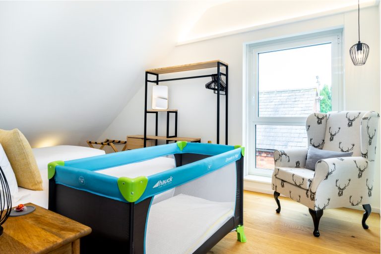 Hauck travel cot in a bright, modern bedroom with a stag-patterned armchair and wooden floor, ideal for families at 14 Acres.