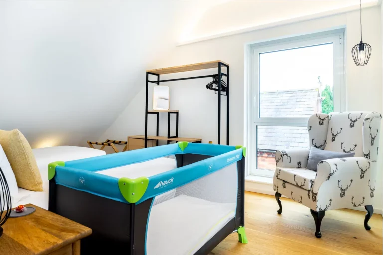 Hauck travel cot in a bright, modern bedroom with a stag-patterned armchair and wooden floor, ideal for families at 14 Acres.