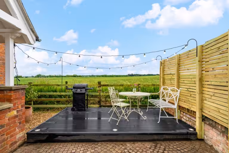 Outdoor patio with black decking, white wrought iron garden furniture, and a BBQ grill, overlooking green fields at 14 Acres.