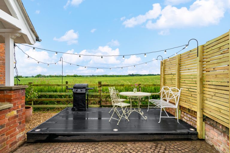 Outdoor patio with black decking, white wrought iron garden furniture, and a BBQ grill, overlooking green fields at 14 Acres.