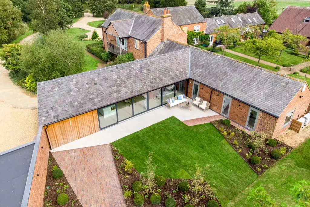 Aerial view of The Barn at 14 Acres, an L-shaped brick barn conversion with a glass wall onto its garden