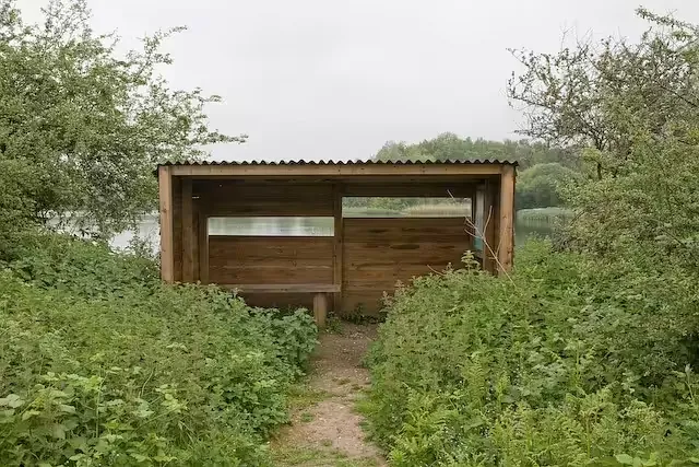 Wooden bird hide among bushes beside a lake