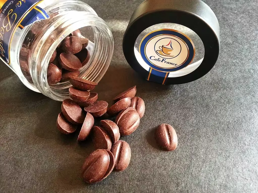 Jar of chocolate-covered coffee beans spilling onto a grey table