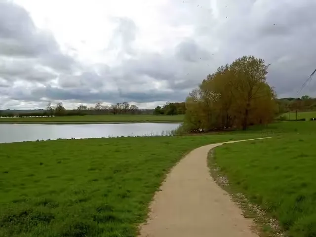 Footpath through grassland beside a reservoir under a cloudy sky