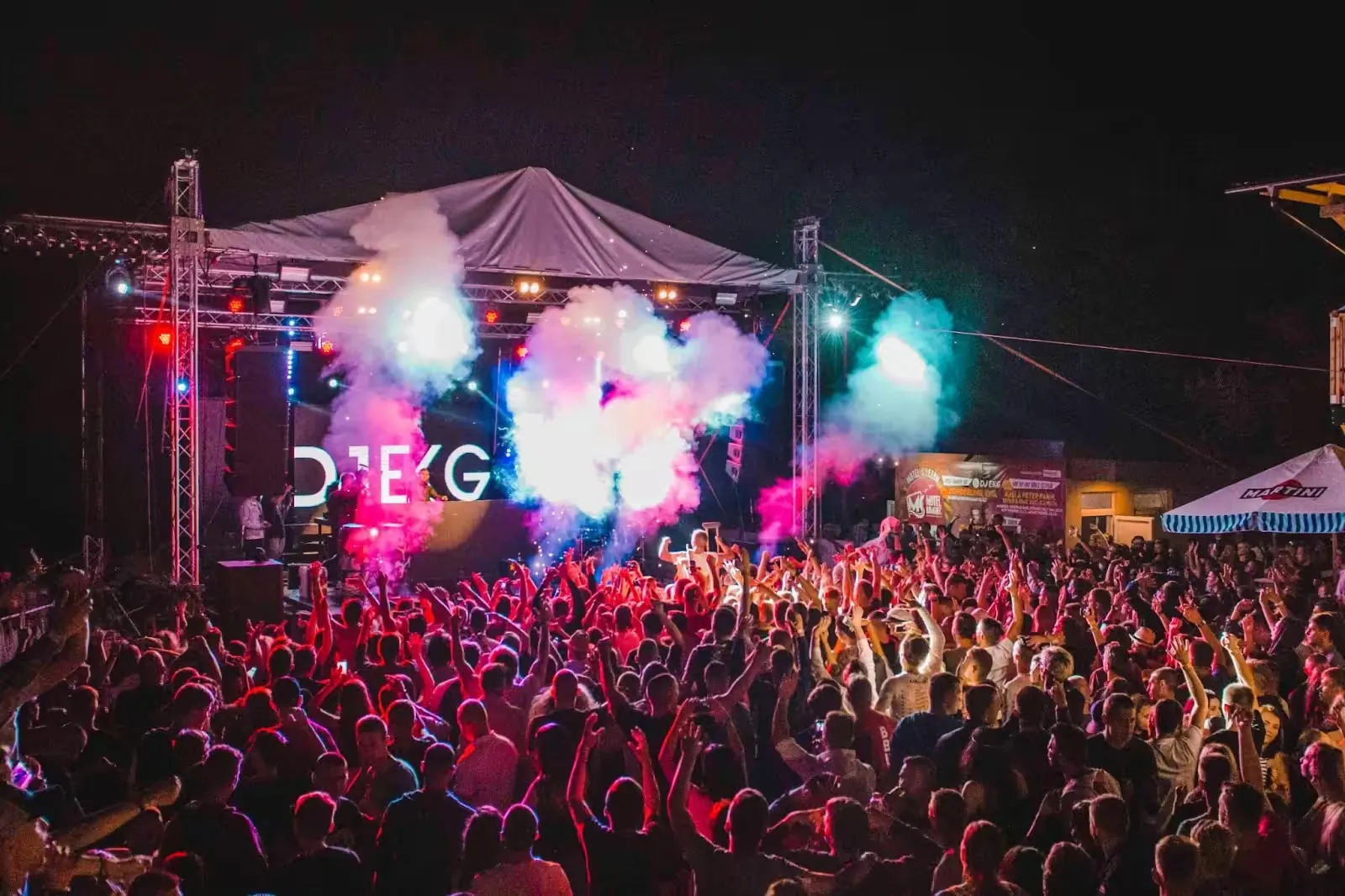 Crowd in front of a festival stage lit with coloured smoke at night