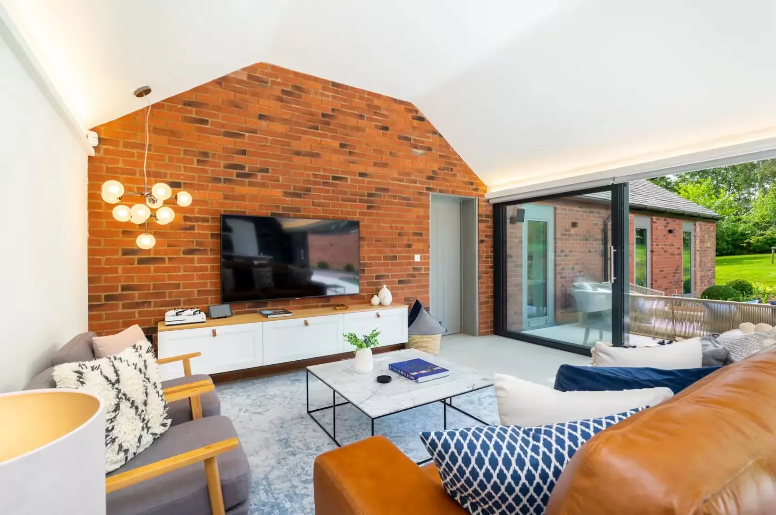 Living room with an exposed brick gable wall, wall-mounted TV and leather sofa, opening onto a terrace