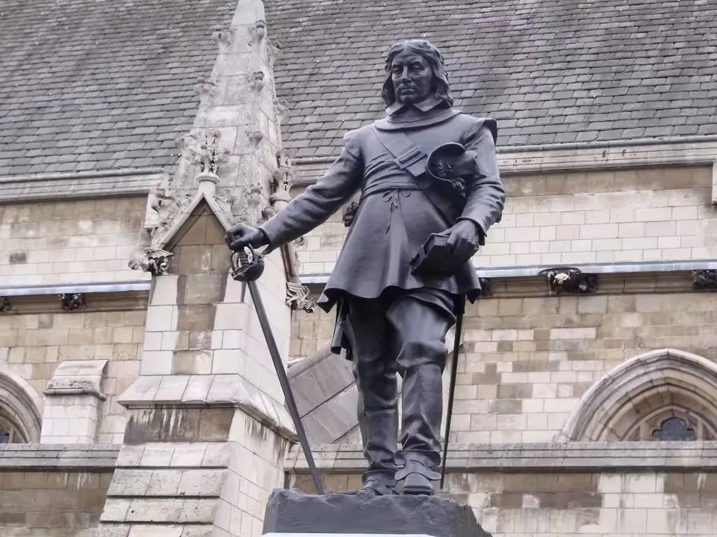 Bronze statue of Oliver Cromwell holding a sword, in front of a Gothic stone building