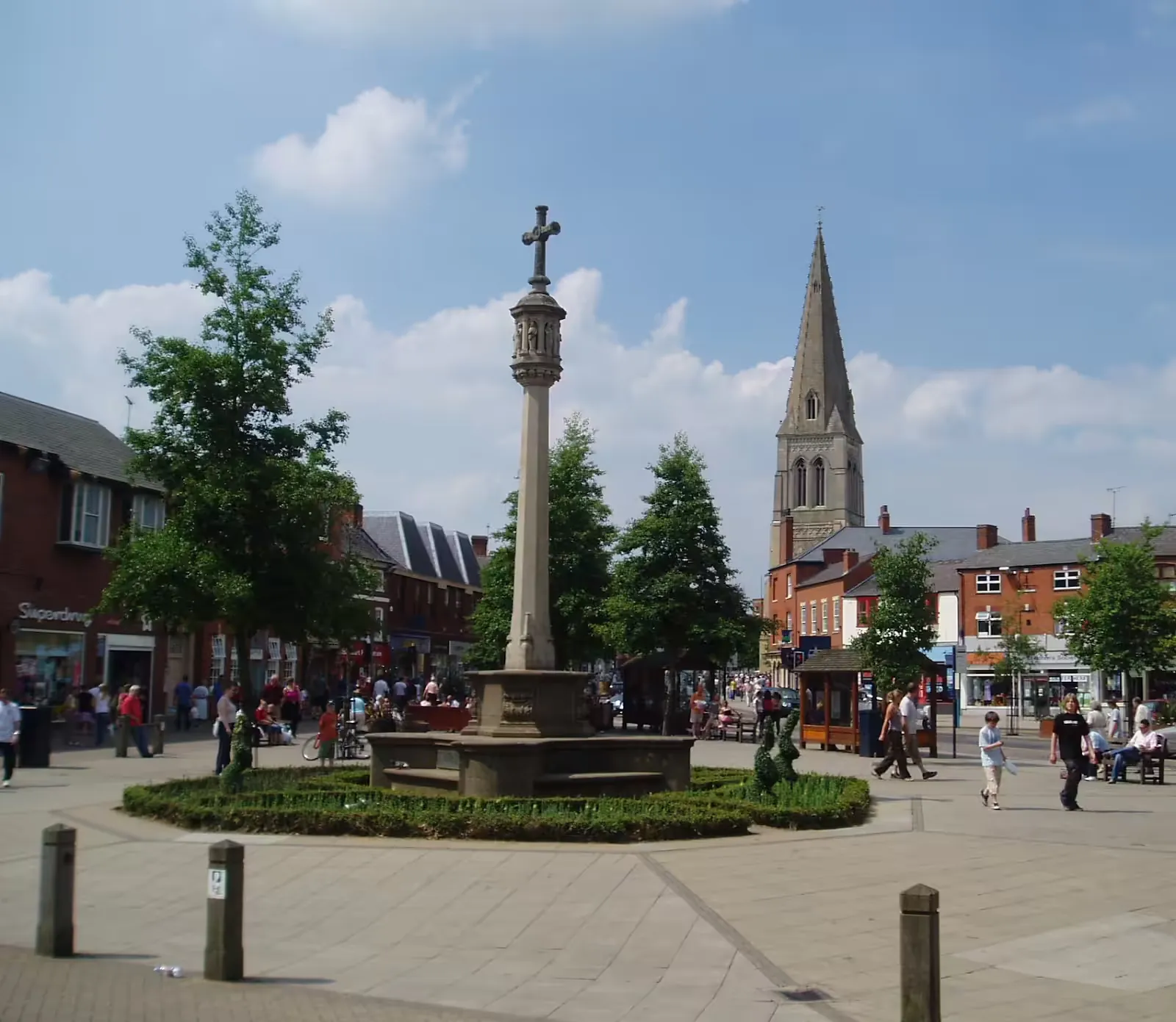 Town square with a stone memorial cross, shops and a church spire