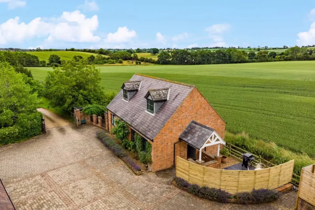 Aerial view of The Cottage at 14 Acres, a red-brick cottage with dormer windows and a fenced terrace beside open fields