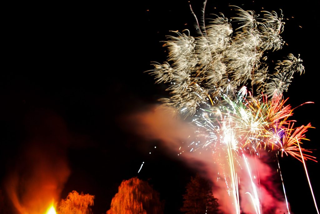 Fireworks bursting above trees beside a village bonfire on a November night in England