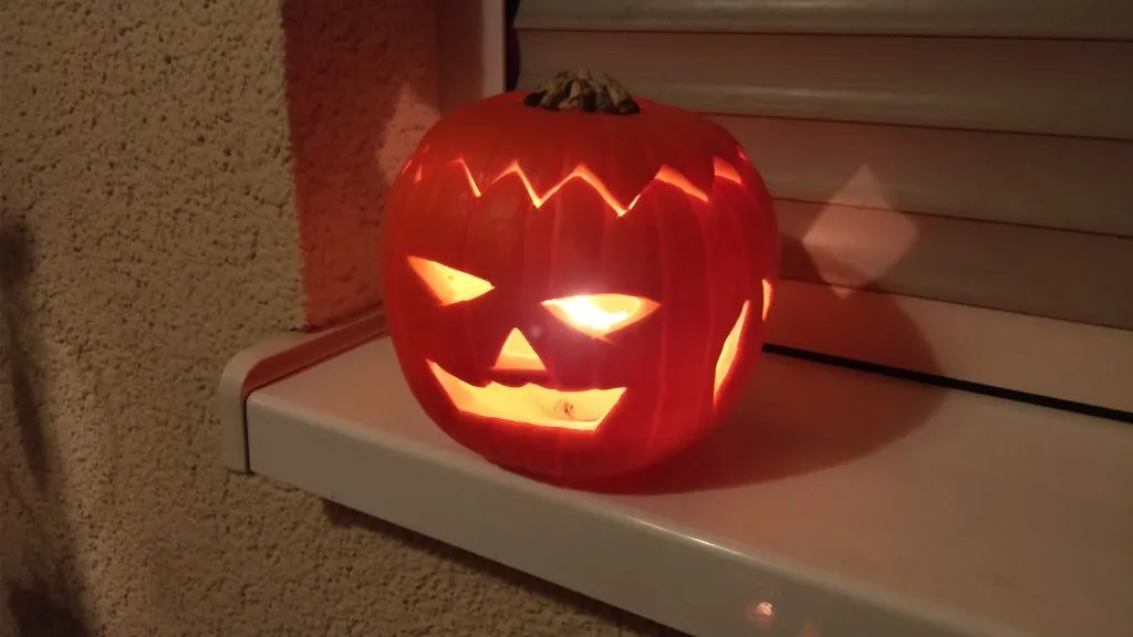 A carved Halloween jack-o'-lantern lit by a candle on a windowsill at night