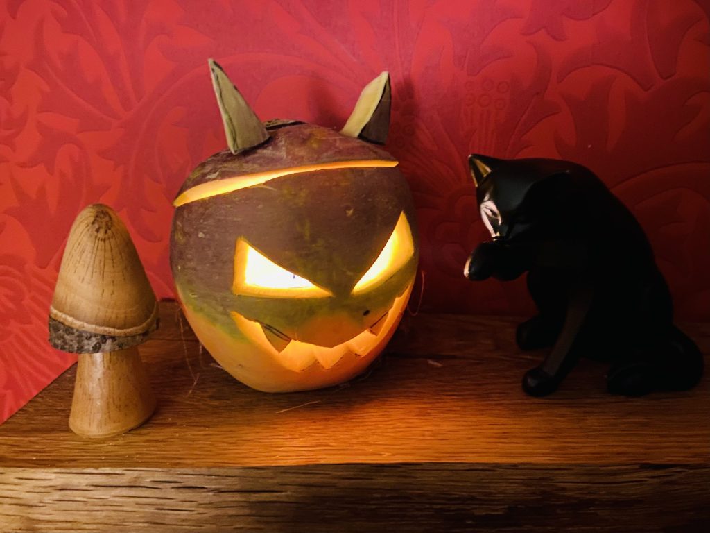 A traditional Scottish Halloween turnip lantern, known as a tumshie, glowing beside a black cat ornament
